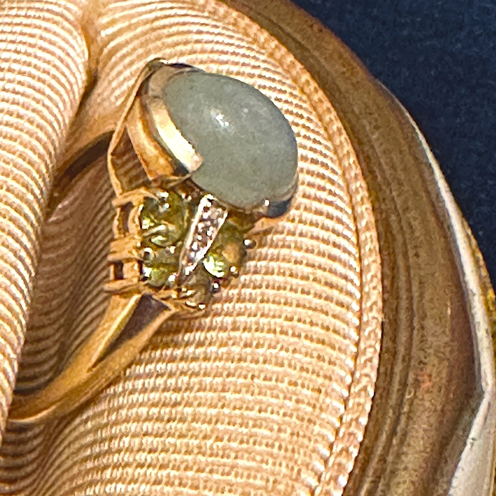 14k gold ring with green stones, clear stones, and a center smooth type stone.